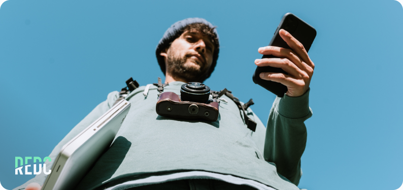 A man with a phone, laptop, and a camera around his neck.