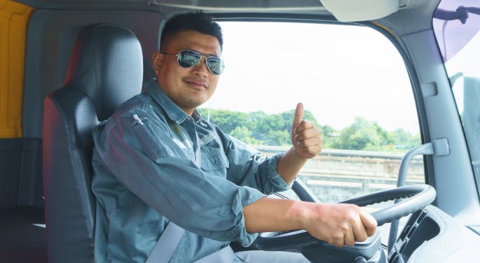A driver behind the steering wheel giving the camera a thumbs up. 
