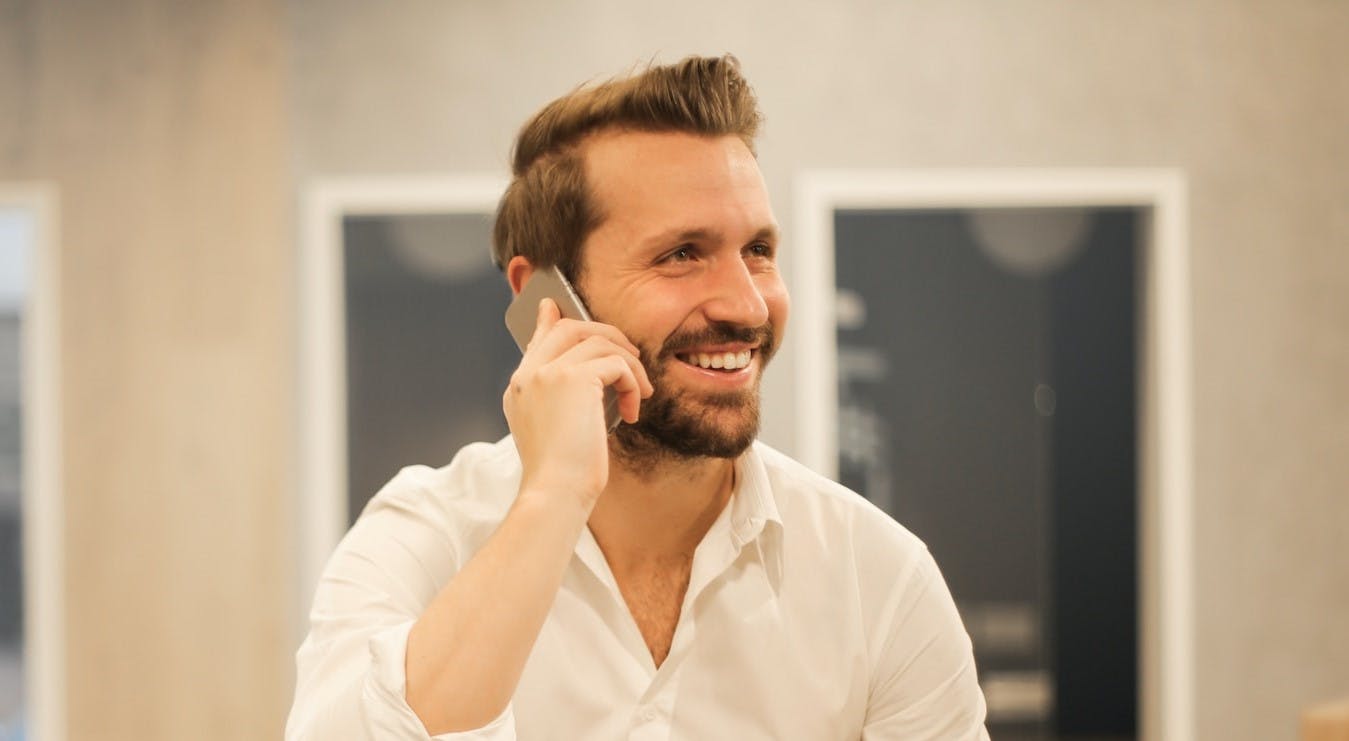 A man wearing a pleasant expression engages in conversation on a mobile phone.