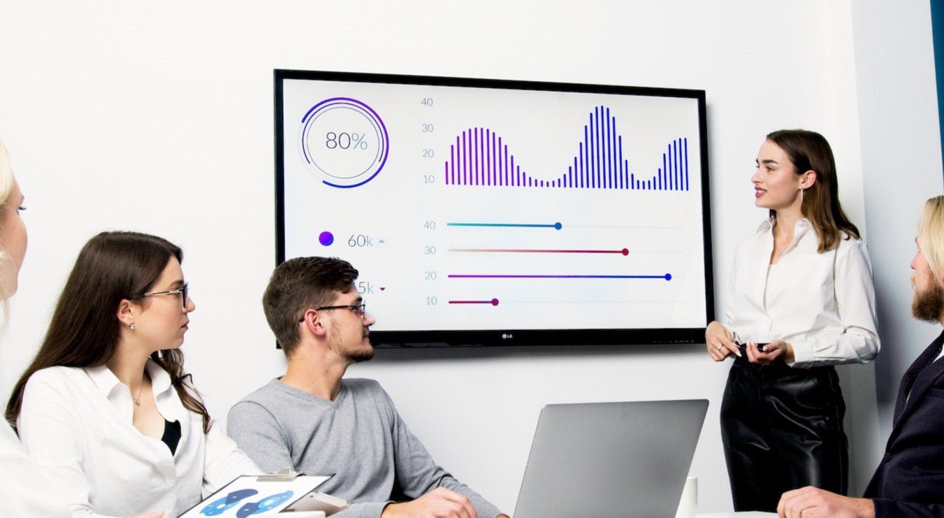 Woman presenting information to colleagues on large monitor